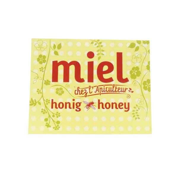 Étiquette jaune clair avec motifs floraux et pois, texte rouge « miel » et « honey », abeille au centre.